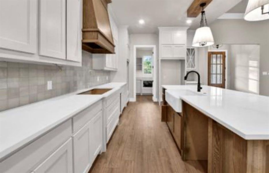 Kitchen with white cabinetry, light countertops, light wood finished floors, decorative backsplash, and a center island with sink