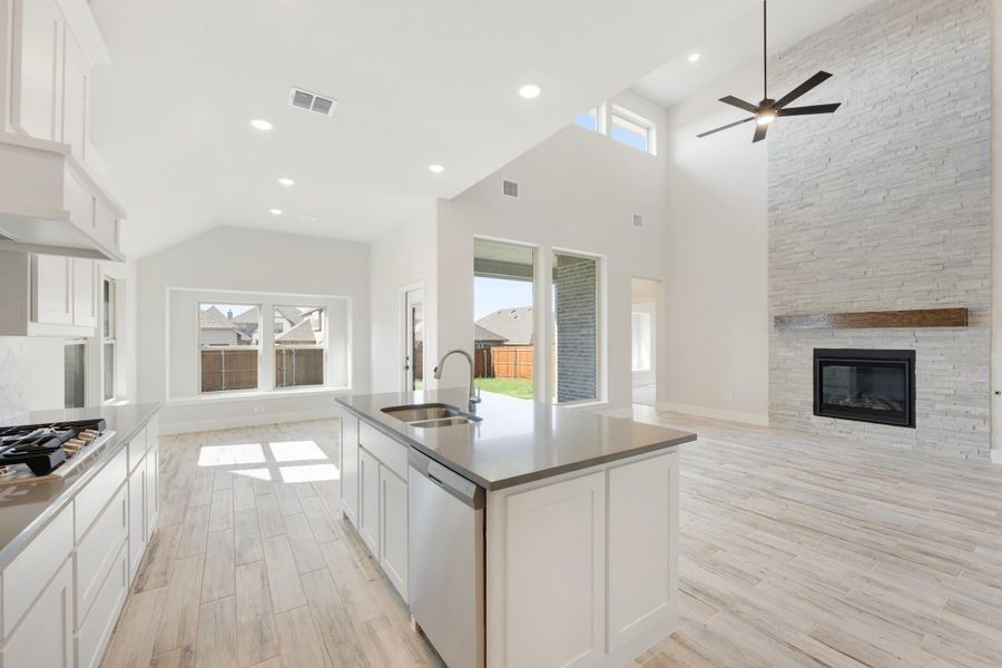 Open-concept kitchen with white cabinets, center island, and stone fireplace under vaulted ceiling Open-concept kitchen with white cabinets, center island, and stone fireplace under vaulted ceiling