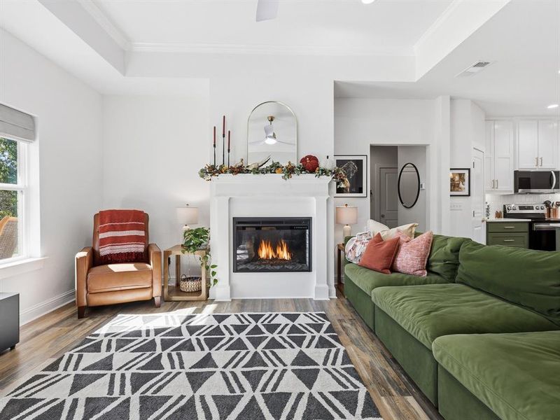 Living room with dark wood finished floors, crown molding, a ceiling fan, recessed lighting, and a glass covered fireplace
