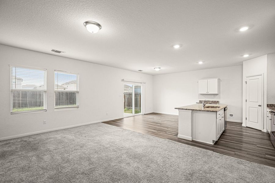 Kitchen with open floor plan, a center island with sink, a textured ceiling, dark stone countertops, and dark carpet