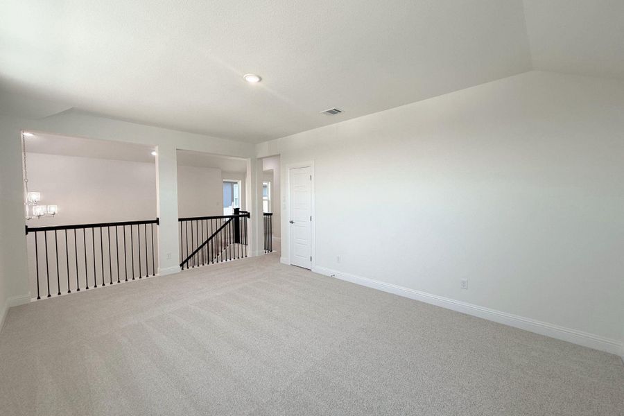 Expansive carpeted area featuring a white door, recessed lighting, and black metal railings overlooking lower levels