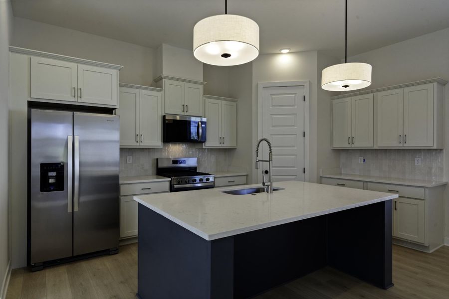 Kitchen featuring a substantial island with a basin sink, stainless steel appliances, light-toned cabinetry, light-colored countertops, and wood-finish flooring