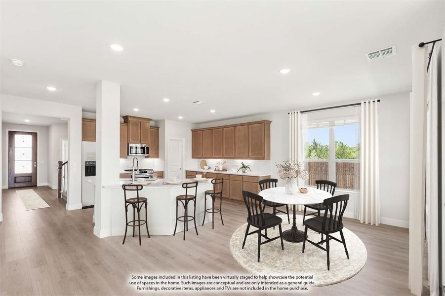Open-concept kitchen and dining area with wood cabinets, island with bar stools, and round dining table on light hardwood floors