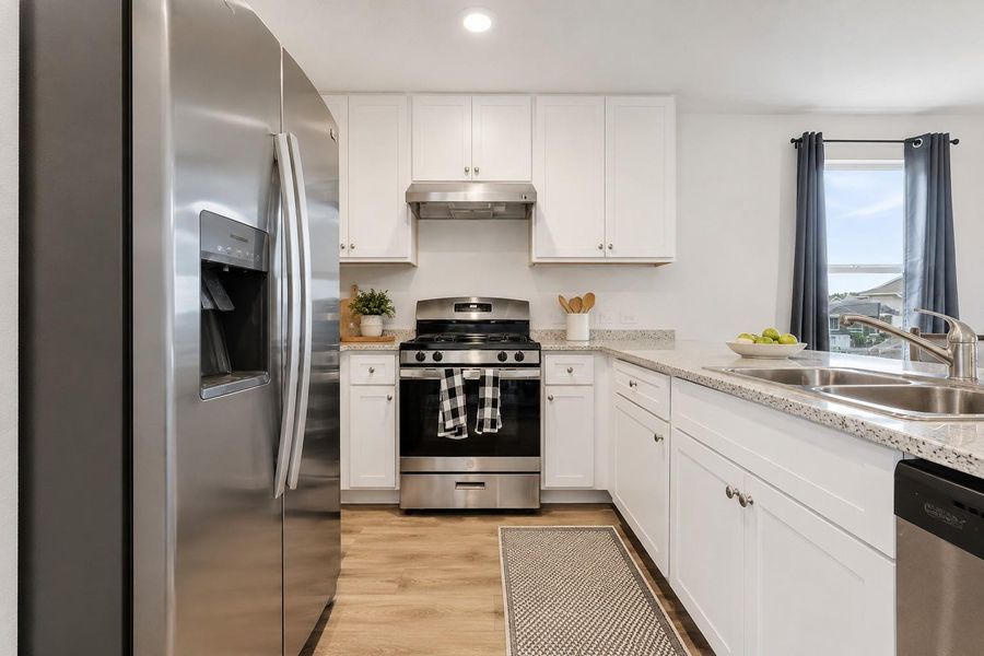 A well-equipped kitchen features white cabinetry and light-toned countertops, complete with modern stainless steel appliances.