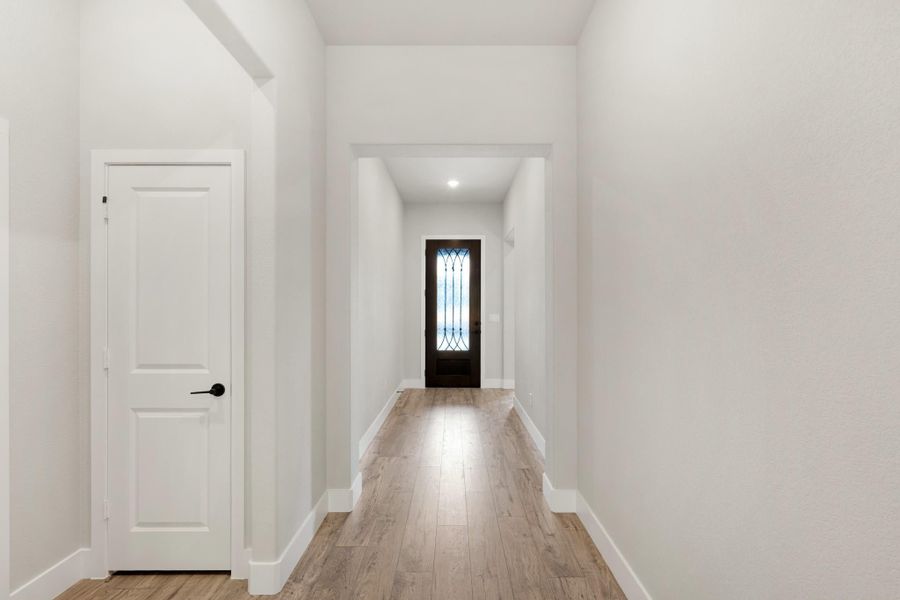Hallway with white walls, light wood floors, and dark wood front door with glass panel