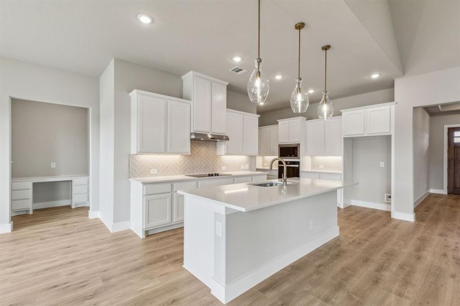 Kitchen featuring built in microwave, sink, white cabinetry, and an island with sink