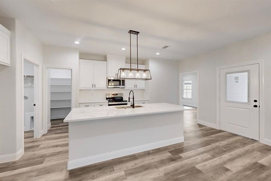 Kitchen featuring sink, white cabinetry, hanging light fixtures, stainless steel appliances, and an island with sink