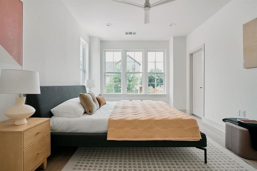 Bright interior room featuring three tall windows, light wood-finish flooring, and a contemporary ceiling fan