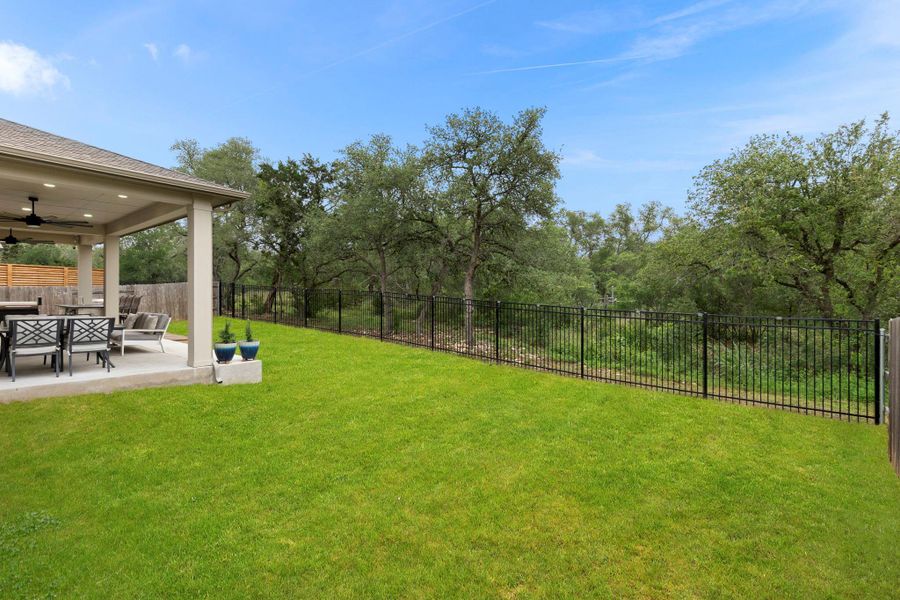 Expansive lawn area featuring a covered patio, black metal fencing, wood privacy fencing, and mature trees