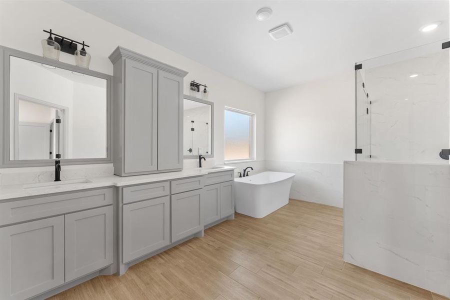 Bathroom featuring double vanity, a marble finish shower, a soaking tub, and light wood finished floors