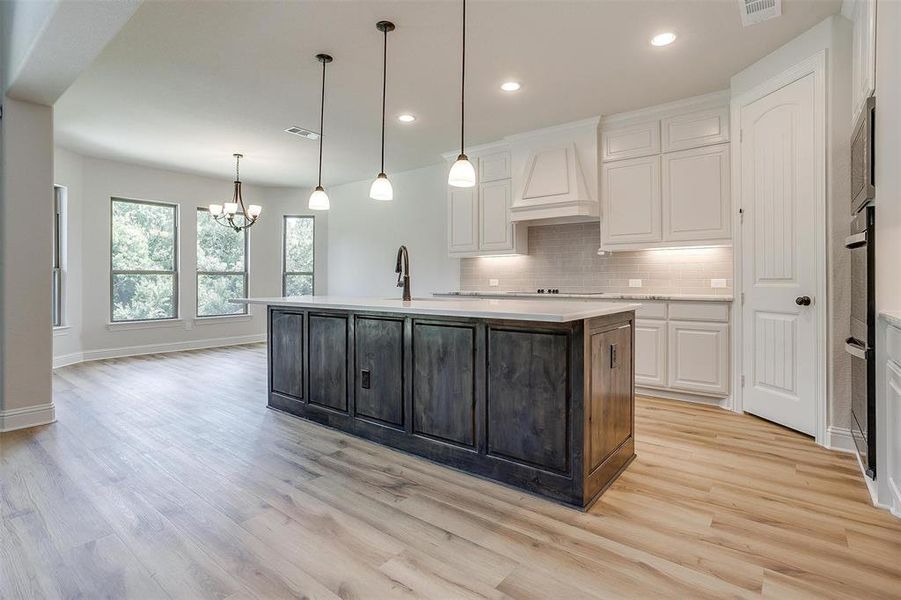 Kitchen with decorative backsplash, light wood-type flooring, a kitchen island with sink, white cabinetry, and custom range hood