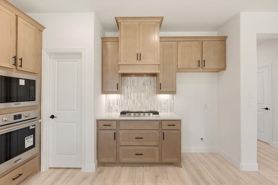 Kitchen with light wood cabinets, gas cooktop, tile backsplash, and built-in double oven with microwave