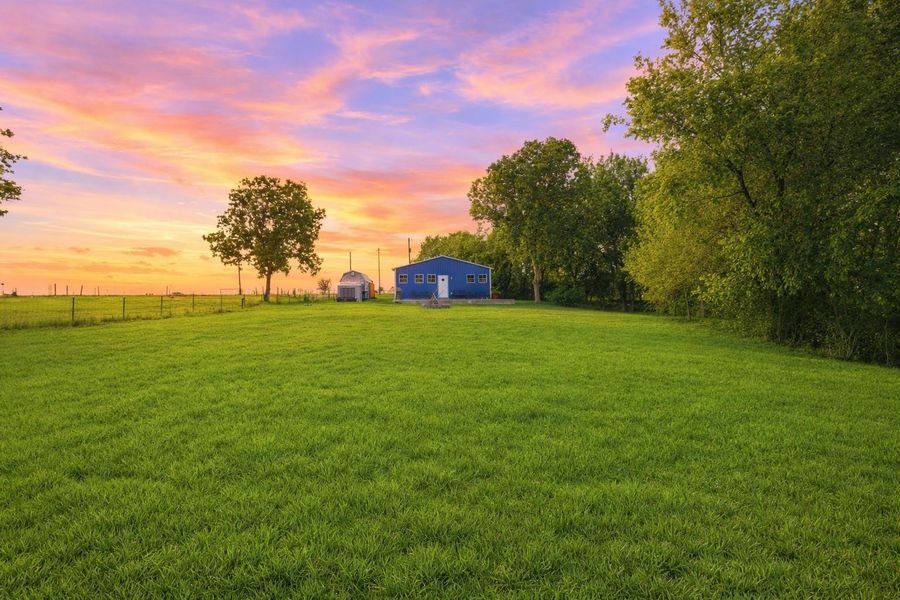 The property features a blue structure and a substantial green lawn, bordered by mature trees