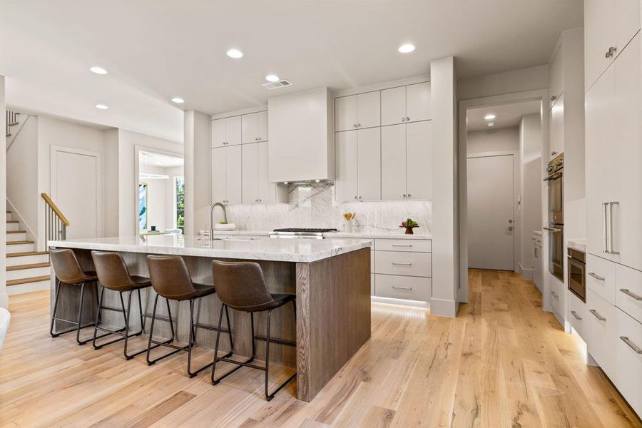 Kitchen with a breakfast bar, a center island with sink, light wood-style flooring, tasteful backsplash, and recessed lighting Kitchen with a breakfast bar, a center island with sink, light wood-style flooring, tasteful backsplash, and recessed lighting