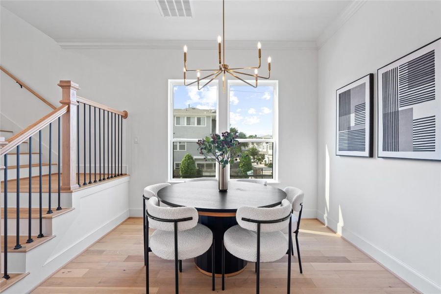 Elegant dining space featuring a modern chandelier, warm wood flooring, and an open layout that seamlessly connects to the kitchen and living areas - perfect for intimate gatherings or entertaining guests.