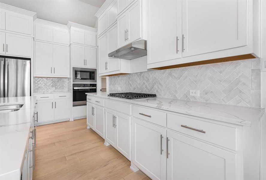 Kitchen with light stone countertops, stainless steel appliances, tasteful backsplash, white cabinets, and under cabinet range hood Kitchen with light stone countertops, stainless steel appliances, tasteful backsplash, white cabinets, and under cabinet range hood