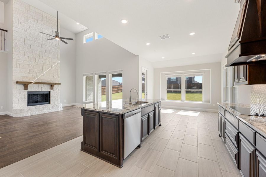 Open kitchen with dark wood island and granite countertops, open to living room with stone fireplace and vaulted ceiling Open kitchen with dark wood island and granite countertops, open to living room with stone fireplace and vaulted ceiling
