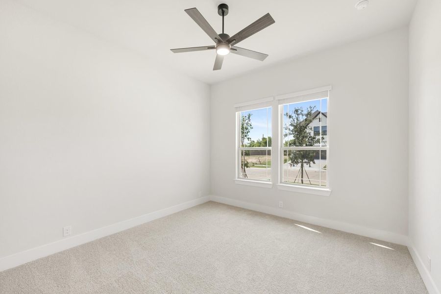 Empty bedroom with white walls, carpet flooring, ceiling fan, and two windows with outdoor views