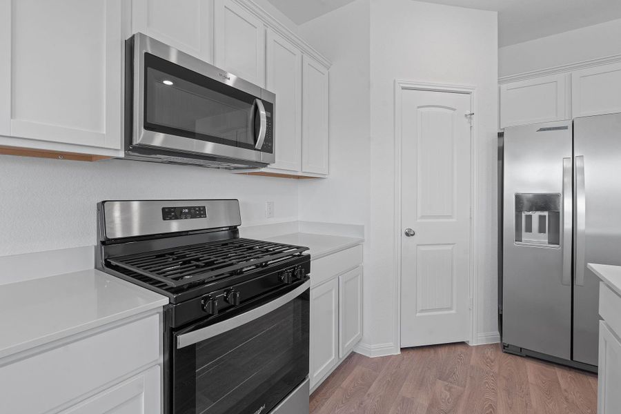 Kitchen featuring appliances with stainless steel finishes, light wood-style flooring, white cabinets, and light stone countertops Kitchen featuring appliances with stainless steel finishes, light wood-style flooring, white cabinets, and light stone countertops