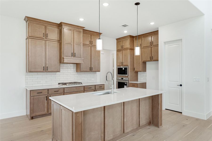 Kitchen with tan wood cabinets, large island with white countertop, pendant lights, and stainless steel appliances Kitchen with tan wood cabinets, large island with white countertop, pendant lights, and stainless steel appliances