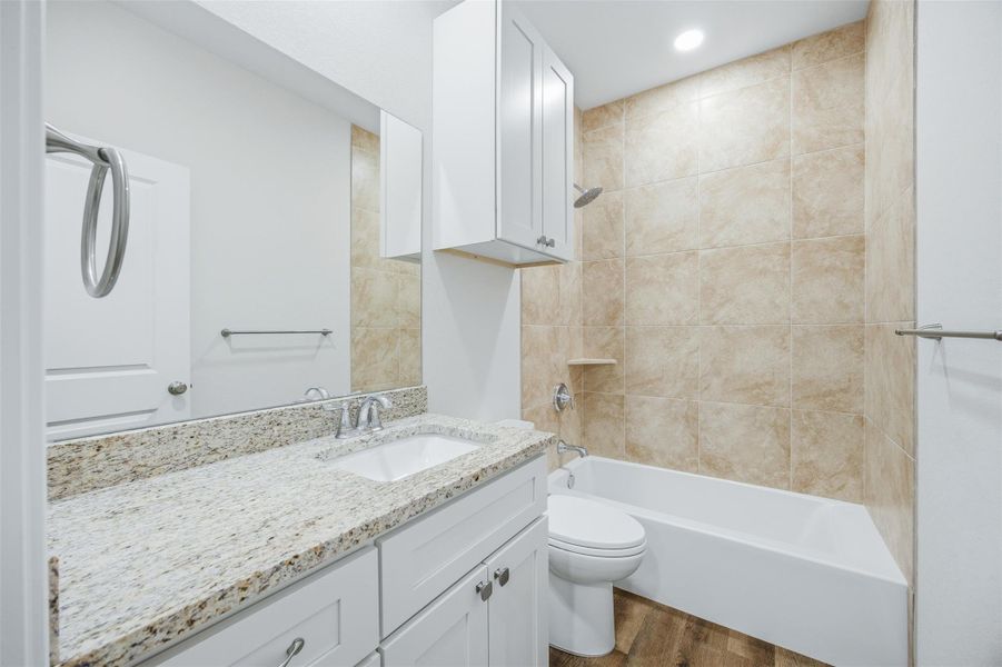 Granite counters and wood flooring elevate this contemporary bathroom with a full bath and shower.