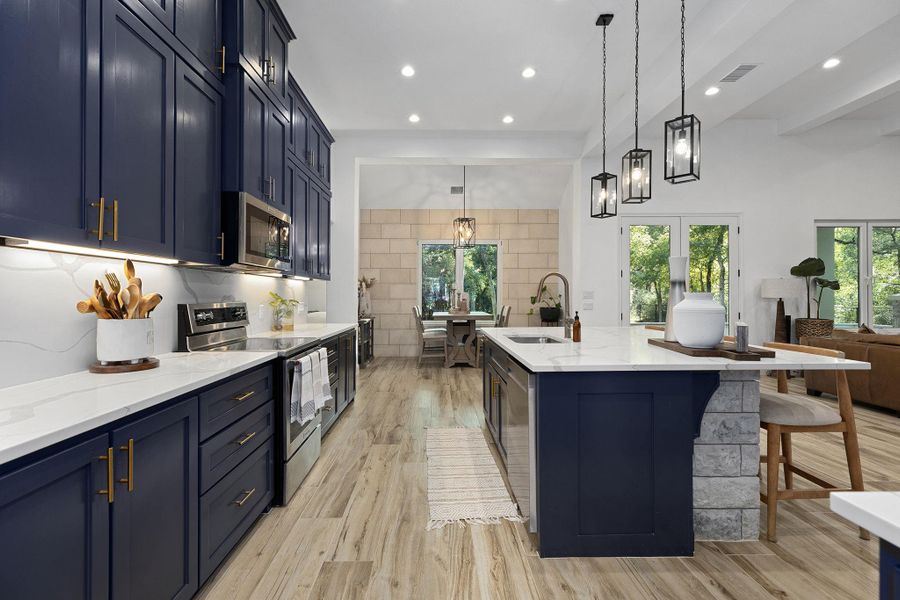 Kitchen featuring blue cabinets, stainless steel appliances, backsplash, pendant lighting, and light stone counters Kitchen featuring blue cabinets, stainless steel appliances, backsplash, pendant lighting, and light stone counters