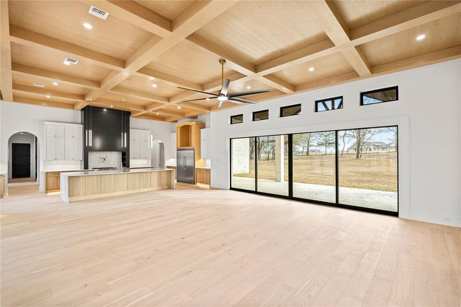 Unfurnished living room with arched walkways, light wood-style floors, coffered ceiling, beamed ceiling, and recessed lighting