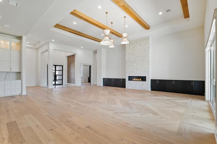 Unfurnished living room with beam ceiling, a high ceiling, a stone fireplace, and recessed lighting