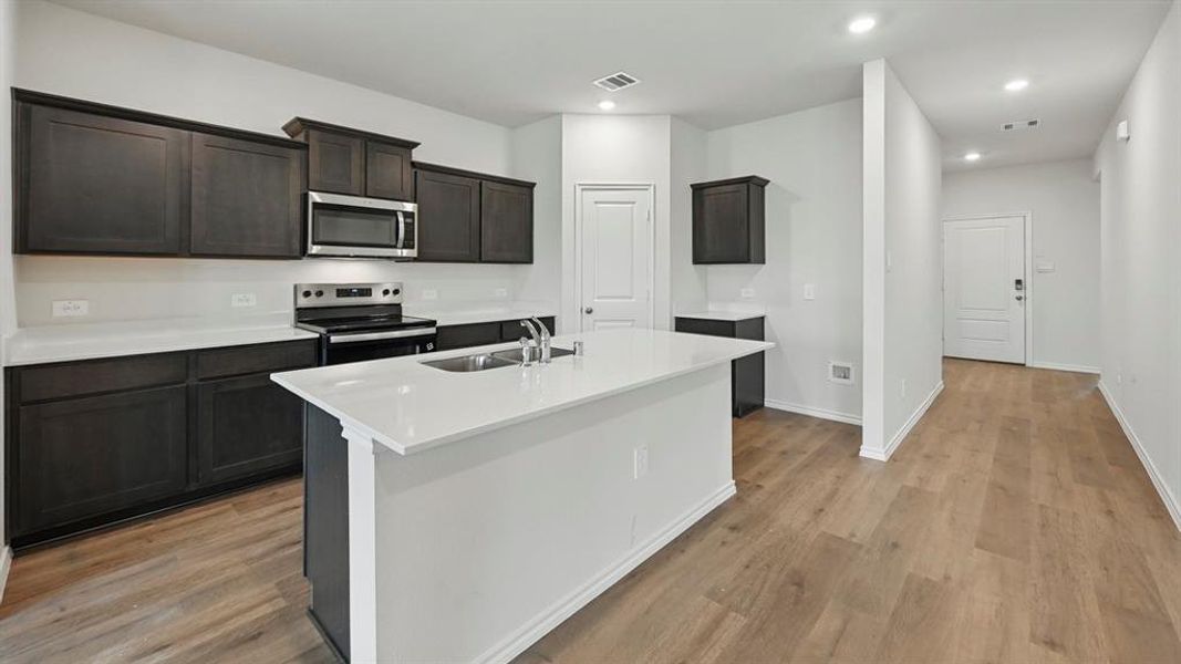 Kitchen with stainless steel appliances, an island with sink, recessed lighting, light wood-style flooring, and light stone countertops