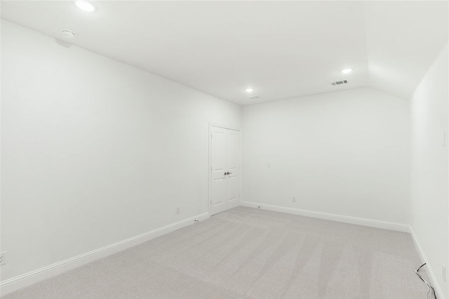 Empty room with white walls, gray carpet, recessed lighting, and a white interior door