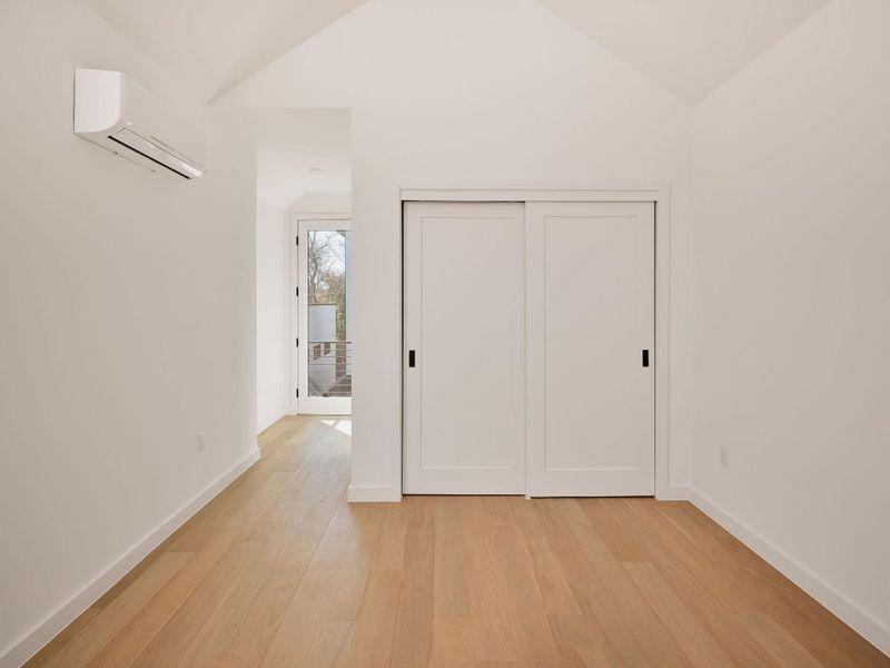 Unfurnished bedroom with vaulted ceiling, light wood-type flooring, a wall mounted air conditioner, and a closet