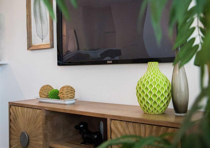 Family room staged with tv mounted on the wall, wooden credenza with vases on top and a house plant obscuring the picture. Family room staged with tv mounted on the wall, wooden credenza with vases on top and a house plant obscuring the picture.