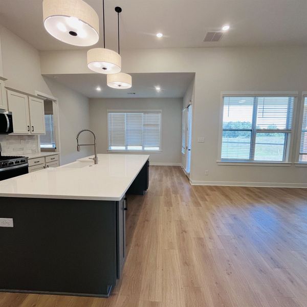 Open concept living area with wood-finish flooring, white cabinetry, dark island with white countertop, and recessed lighting Open concept living area with wood-finish flooring, white cabinetry, dark island with white countertop, and recessed lighting