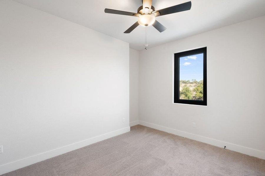 Light-filled room featuring a dark-framed window, neutral carpeting, white baseboards, and a ceiling fan with integrated lighting