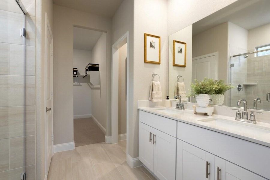 This bathroom features a double vanity with white cabinetry and chrome fixtures, a large mirror, and tiled flooring