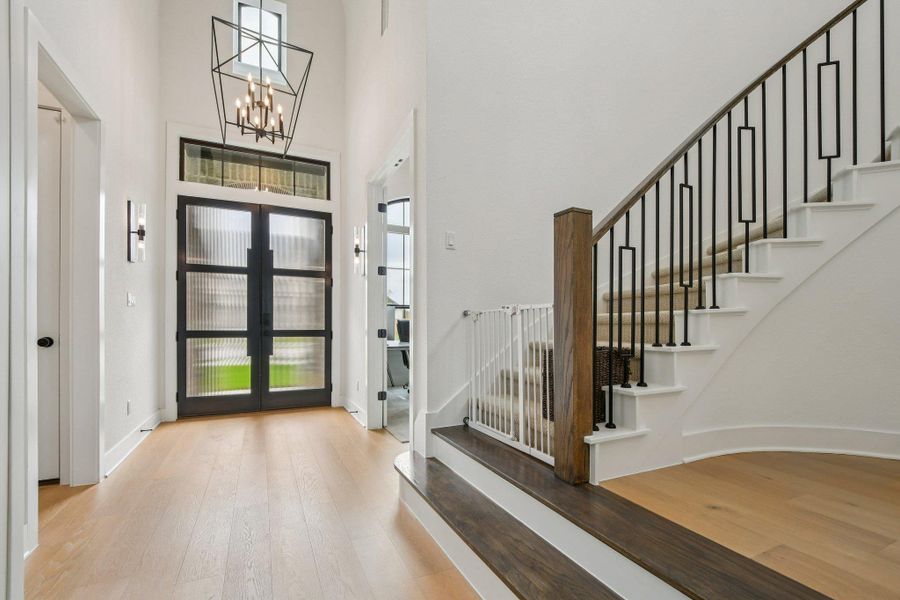Foyer with light wood flooring, a grand entrance door with glass panels, and a staircase featuring black metal spindles and a wood handrail Foyer with light wood flooring, a grand entrance door with glass panels, and a staircase featuring black metal spindles and a wood handrail