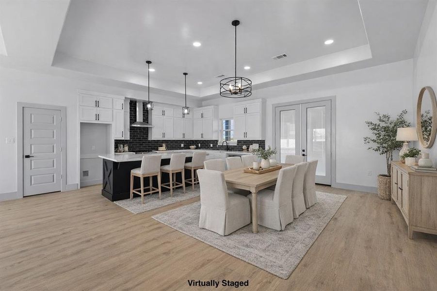 Dining room with a tray ceiling, light wood-style flooring, french doors, and recessed lighting