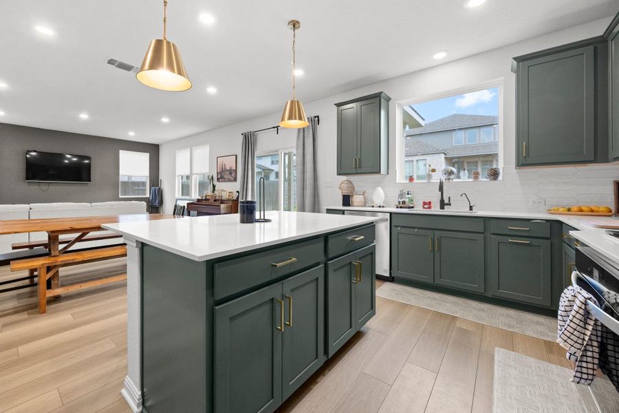 Modern kitchen featuring a central island with a white countertop and dark green cabinetry, complemented by brass pendant lighting
