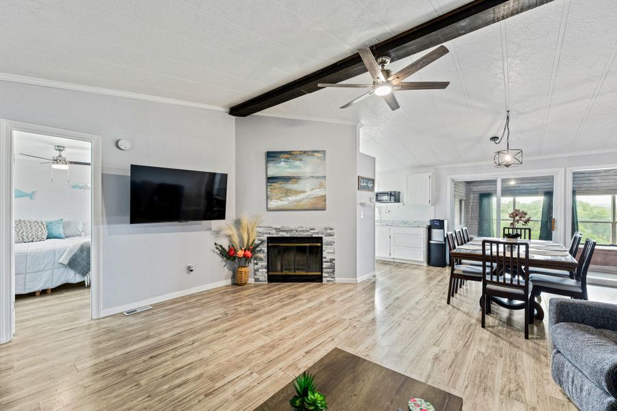 Spacious living area featuring wood-finish flooring, a stone-accented fireplace, and an exposed beam ceiling