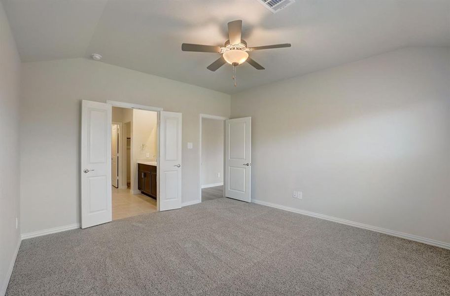 Unfurnished bedroom featuring vaulted ceiling, light colored carpet, ensuite bath, and ceiling fan