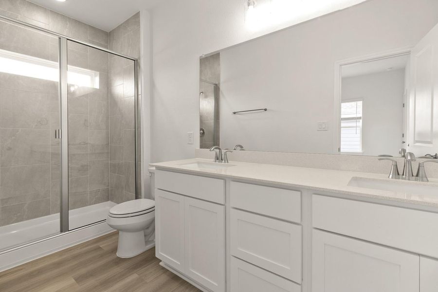Full bathroom featuring healthy amount of natural light, double vanity, a stall shower, and light wood-style flooring