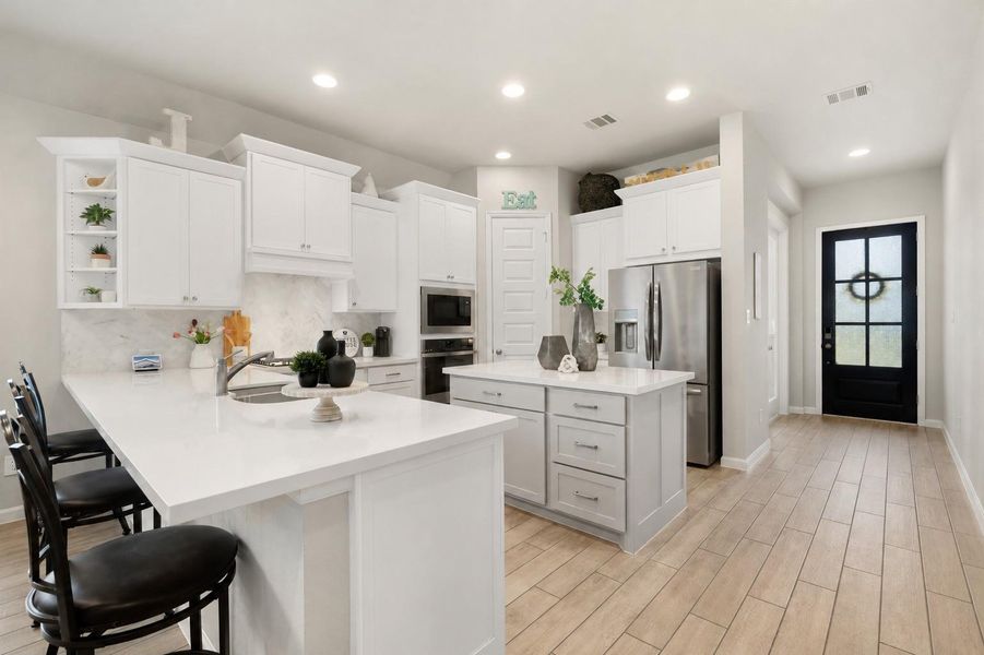 Chef’s kitchen featuring two oversized islands, white cabinetry, & stainless steel appliances.