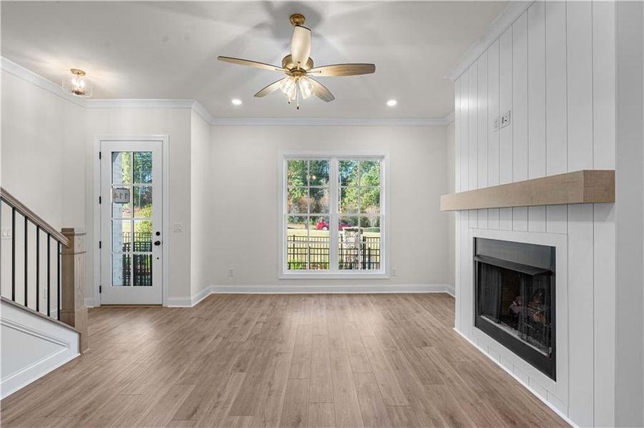 Unfurnished living room with ornamental molding, a fireplace, light wood finished floors, stairway, and recessed lighting