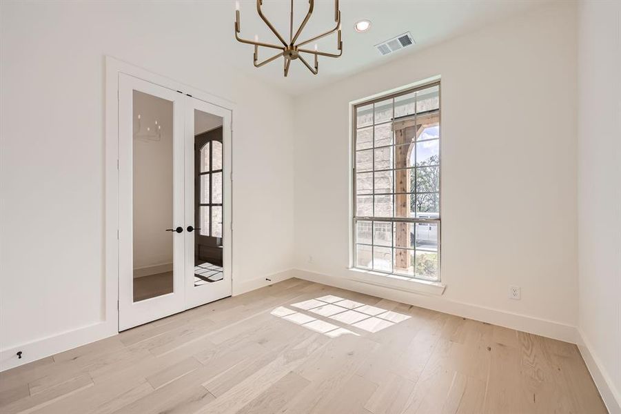 Empty room featuring french doors, a notable chandelier, and light wood-type flooring