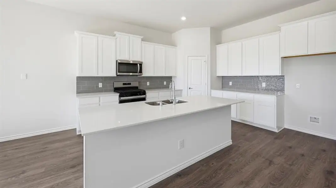 Kitchen featuring white cabinetry, stainless steel appliances, an island with sink, tasteful backsplash, and light stone countertops