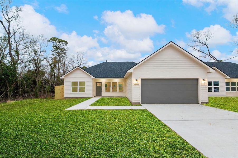 This is a modern, single-story home with a light exterior and dark roof, featuring a spacious two-car garage. It has a well-maintained front lawn and is set against a backdrop of trees, offering a blend of privacy and curb appeal. Lawn is a rendering in this photo