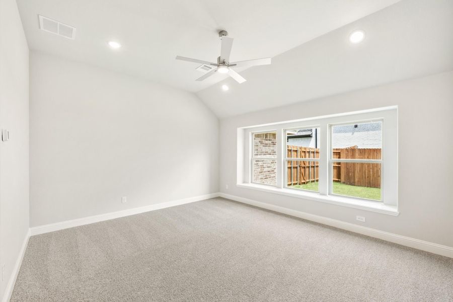 Empty bedroom with vaulted ceiling, ceiling fan, carpet flooring, and large window overlooking backyard fence Empty bedroom with vaulted ceiling, ceiling fan, carpet flooring, and large window overlooking backyard fence
