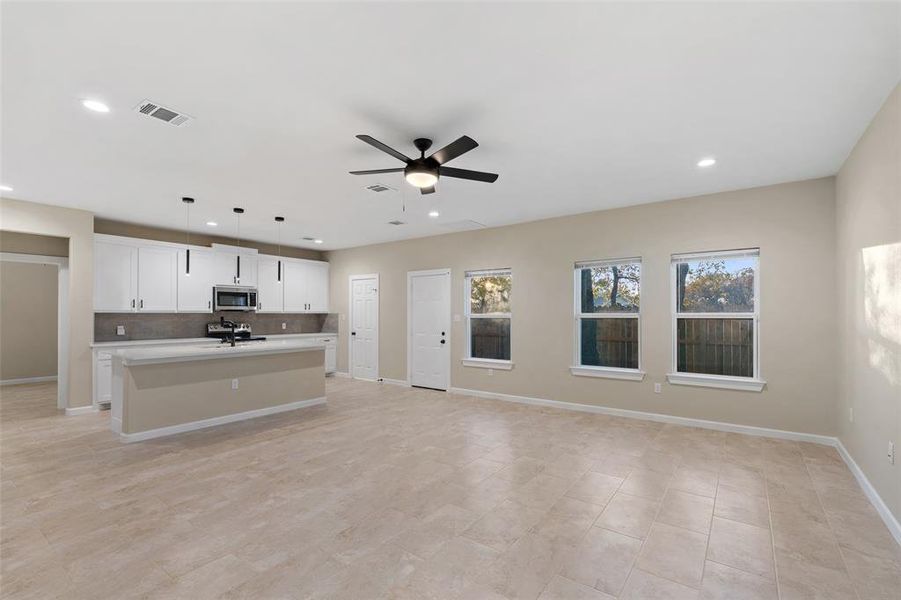 Kitchen with ceiling fan, hanging light fixtures, tasteful backsplash, an island with sink, and white cabinets