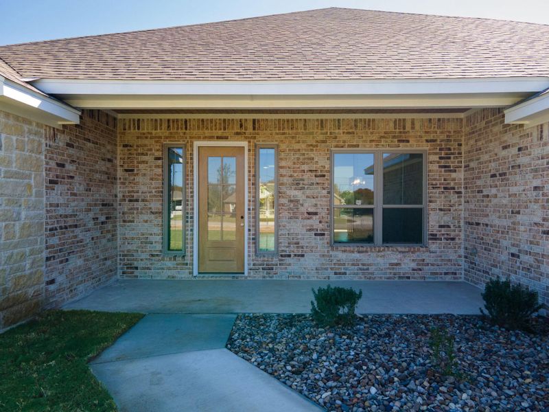 Property entrance featuring brick siding, a patio, and a shingled roof