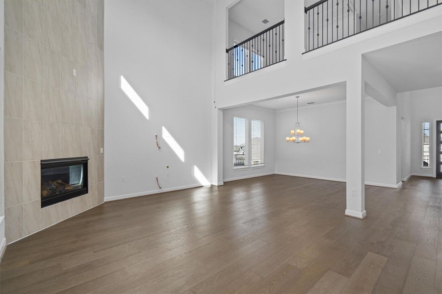 Unfurnished living room with a fireplace, a high ceiling, dark wood-style flooring, and suspended lighting Unfurnished living room with a fireplace, a high ceiling, dark wood-style flooring, and suspended lighting
